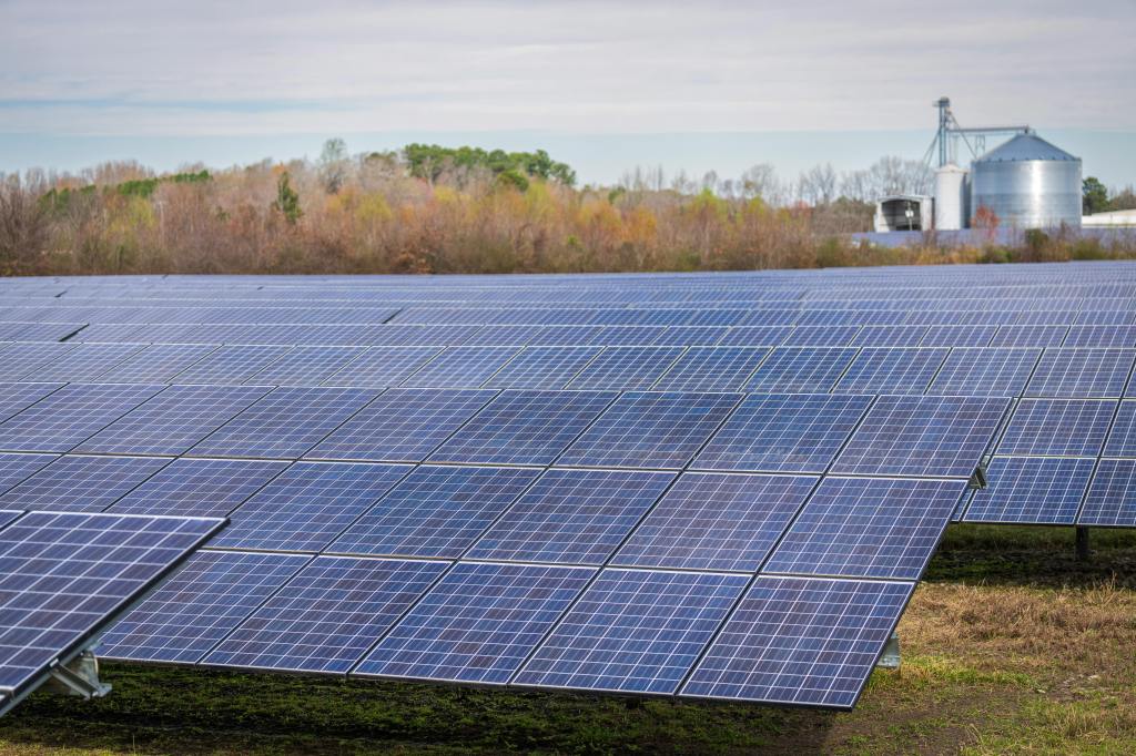 Rows of solar panels in a Michigan solar farm near rural industrial buildings, generating renewable energy for sustainable power solutions