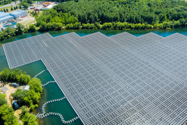 Aerial view of a large floating solar panel system on a reservoir in Michigan, surrounded by lush greenery and nearby facilities, showcasing renewable energy solutions.